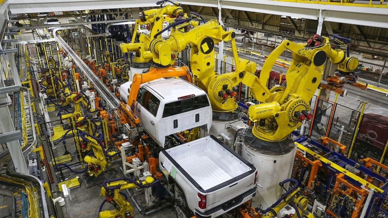 Yellow industrial robots assembling pickup truck bodies on a modern automotive production line
